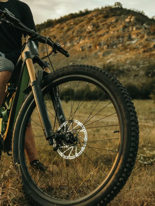 Mies ajaa maastopy&ouml;r&auml;ll&auml; luonnossa, taustalla kukkula ja pilvinen taivas.