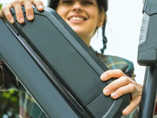 Nainen asettaa akun s&auml;hk&ouml;py&ouml;r&auml;&auml;n, hymyillen.